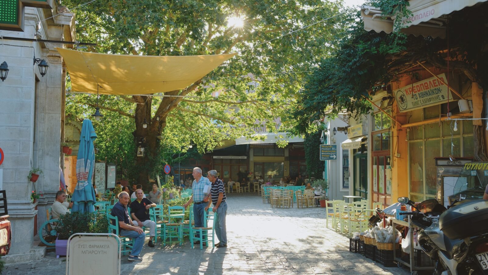 Elderly people sitting on colorful chairs at Agiassos town square, Lesvos, during sunset