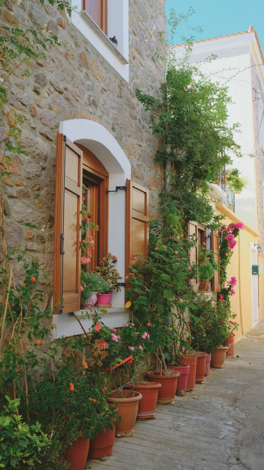 Stone house in Mantamados, Lesvos, decorated with colorful flower pots and plants outside.