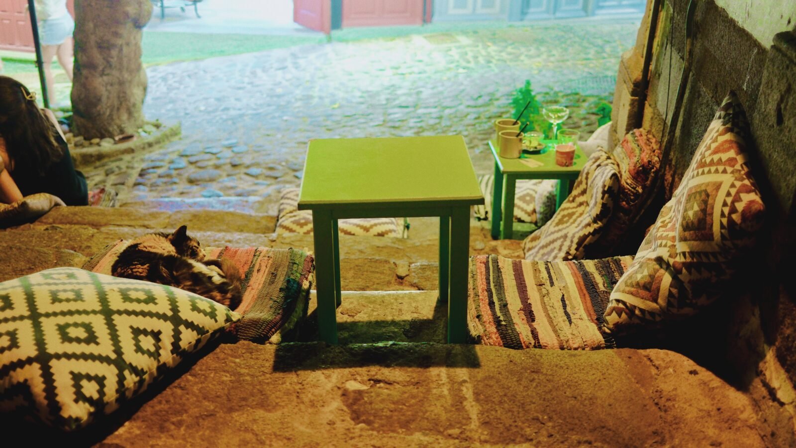 Sleeping cat on cushions beside a small green table at Symposion Bar in Molyvos
