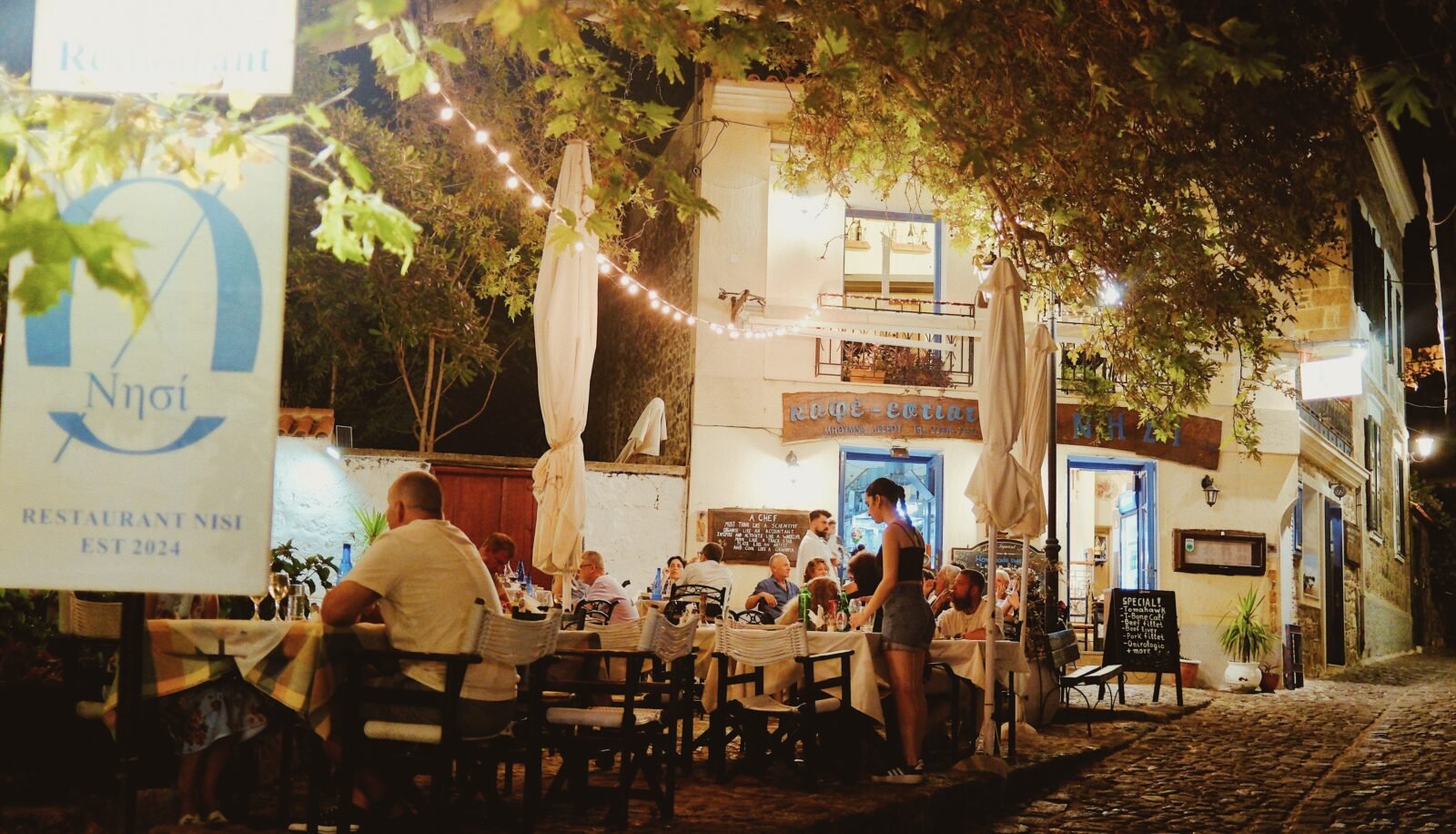 Outdoor dining at Restaurant Nisi in Molyvos, Lesvos, with string lights over a cobblestone street